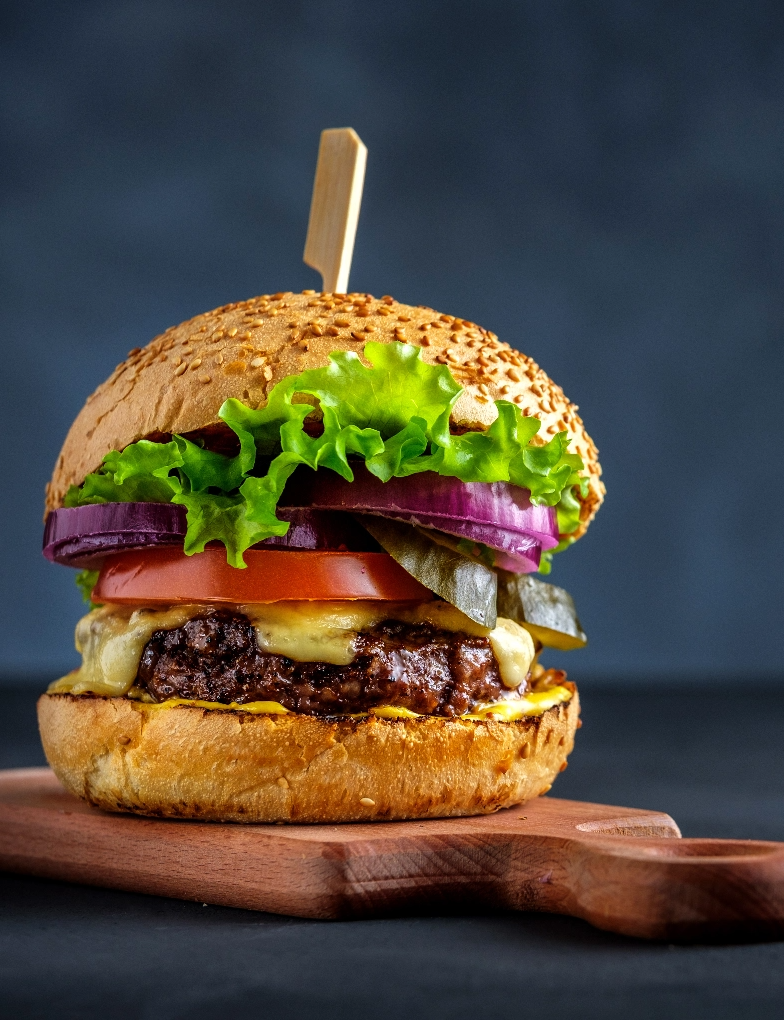 A big hamburger with plenty of fresh veggie toppings on a wooden serving board