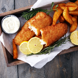 Fish and chips in a basket served with lemon slices and tartar sauce.