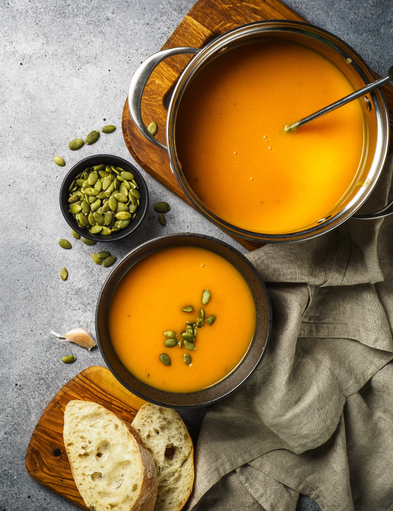 Bowls of bright orange pumpkin soup with pumpkin seeds and bread on the side.