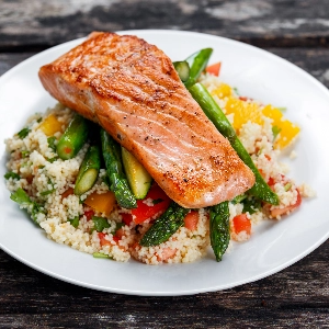 A plate of grilled salmon over rice and vegetables.
