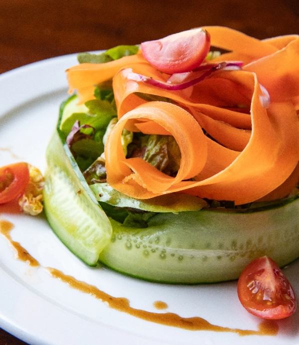 Fresh, thinly sliced veggies make up a salad garnished with tomato and dressing.