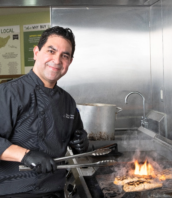 Un chef en uniforme noir grille la viande dans une cuisine.