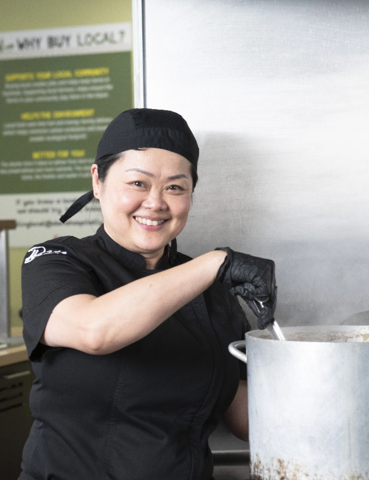 Female chef stirs a large pot of food in a kitchen.