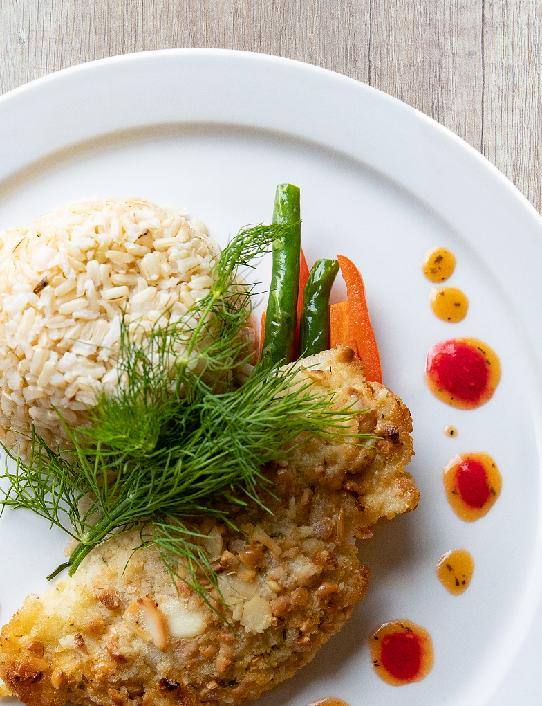 An artfully plated meal of crusted chicken, brown rice and vegetables.