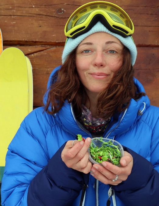 A woman in ski gear eats from a small container of fresh greens